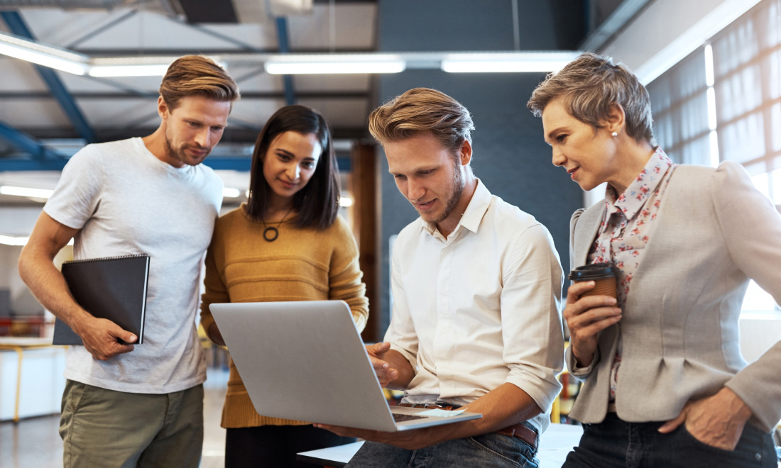 two men and two women in a business setting looking at an open laptop